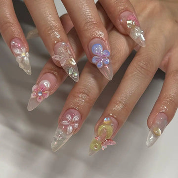 Hand model with long, almond-shaped press-on nails featuring 3D floral and butterfly designs in pastel colors.