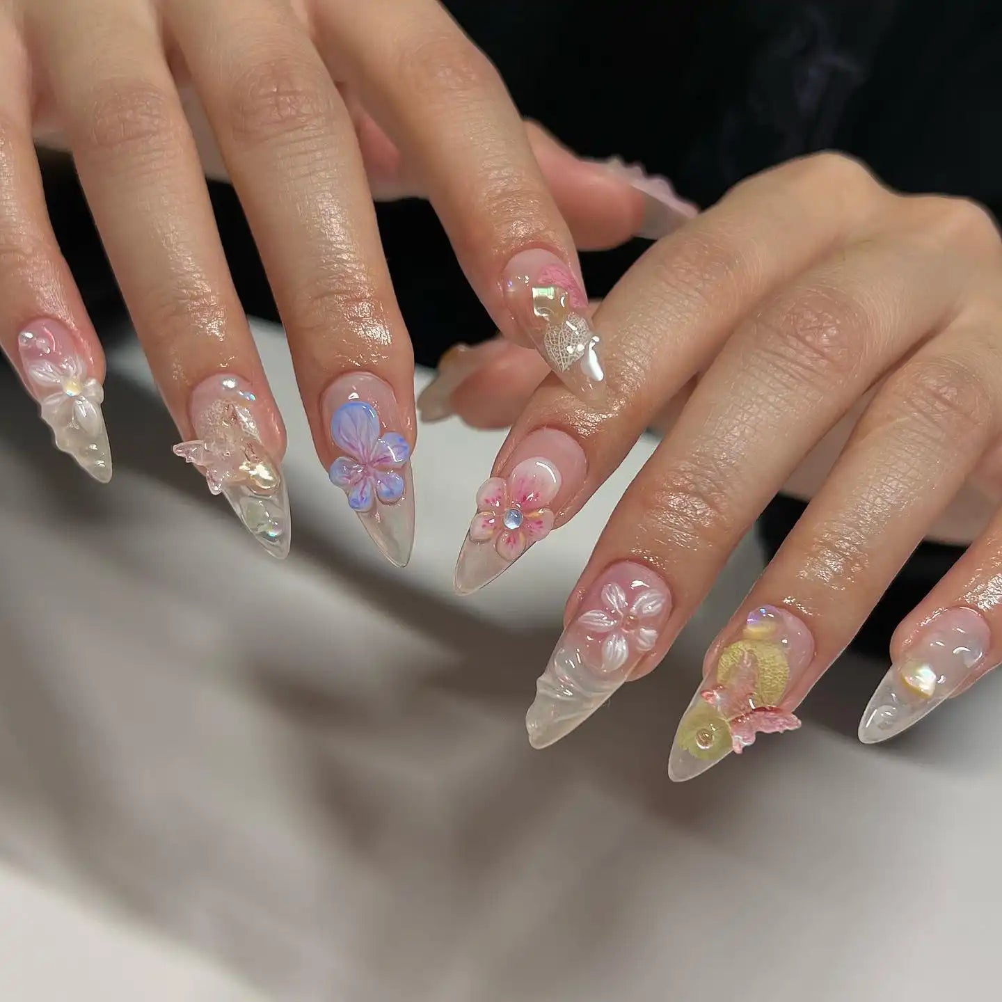 Hand with long clear press-on nails featuring 3D floral and butterfly spring designs