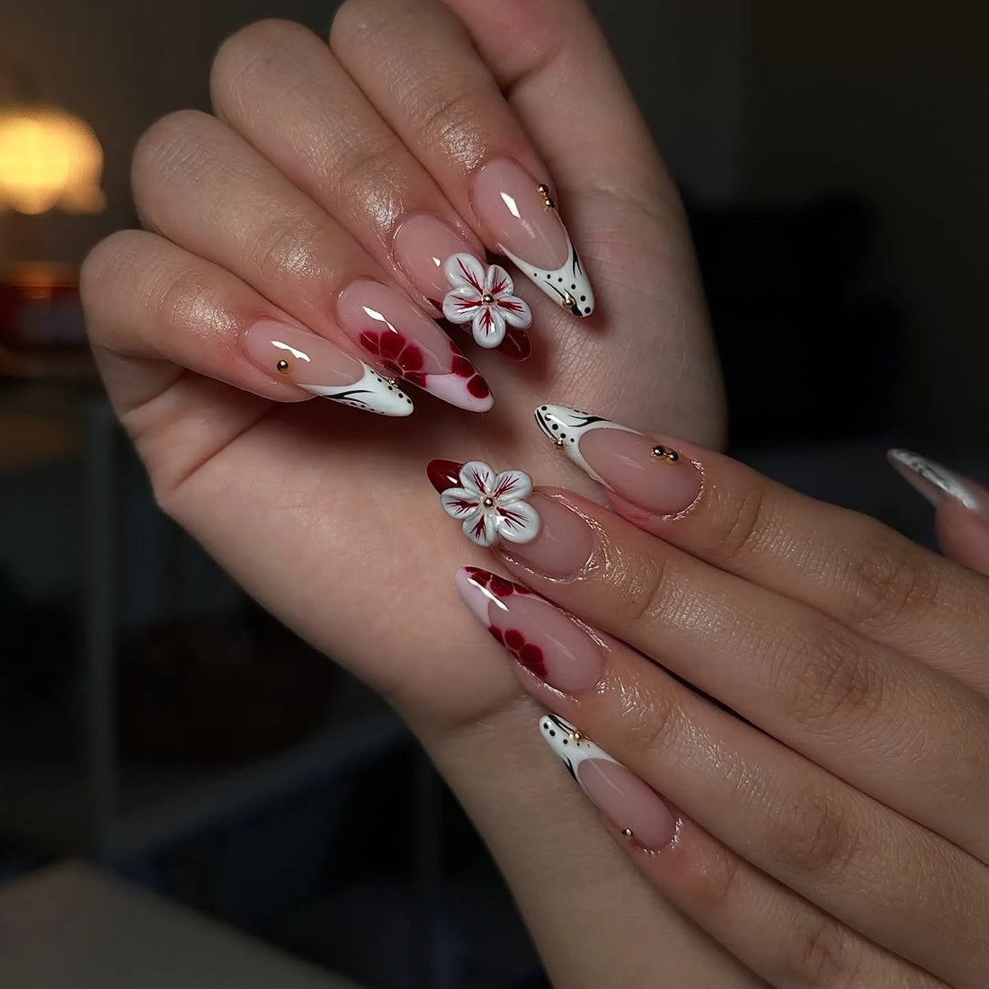 Hand holding handmade press-on nails with 3D red and white flowers, black dot French tips
