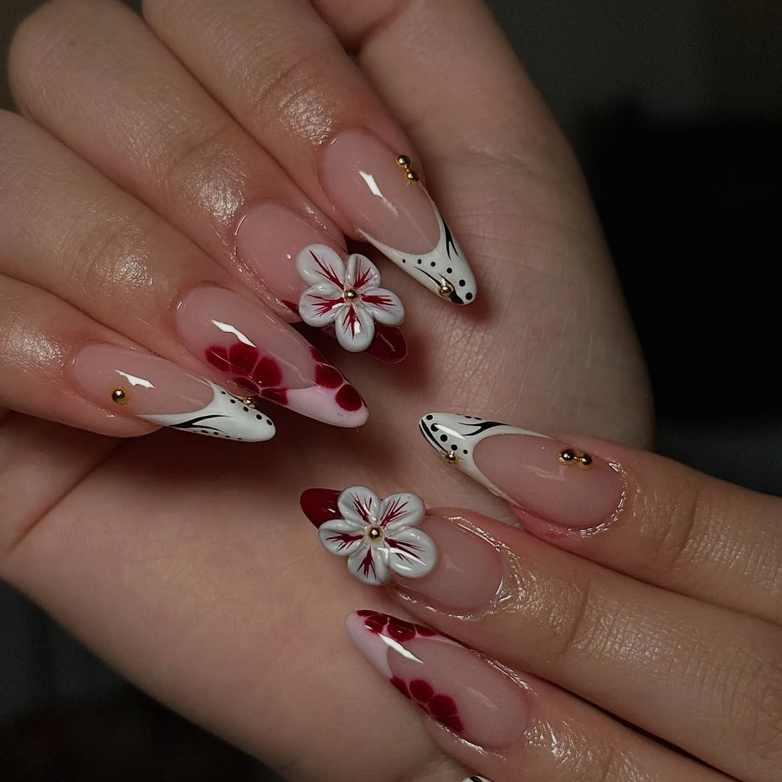 Hand holding handmade press-on nails with 3D red and white flowers, black dot French tips