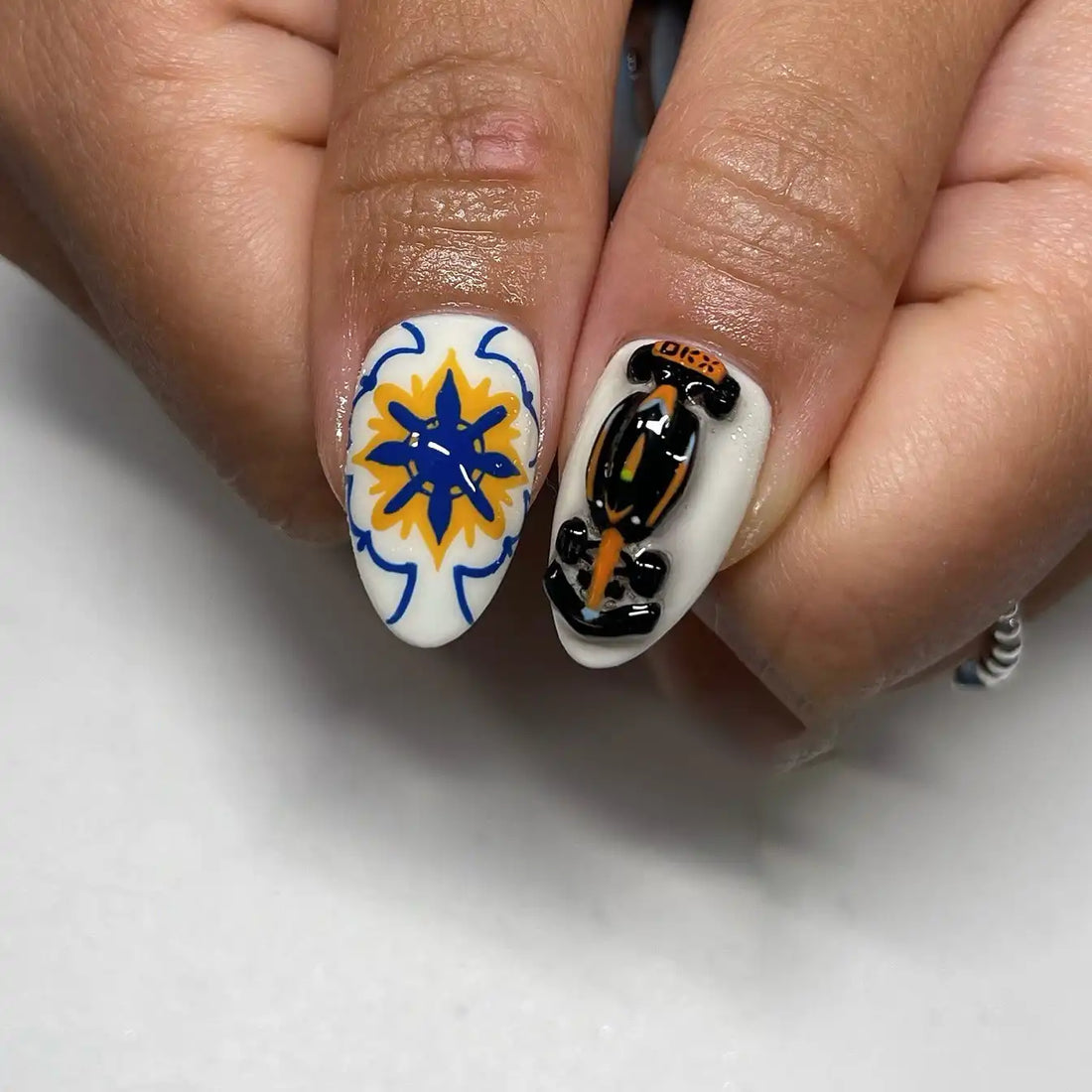 Hand with blue and white 3D floral summer vacation press-on nails featuring lemon, hibiscus, seashell, and ocean designs.