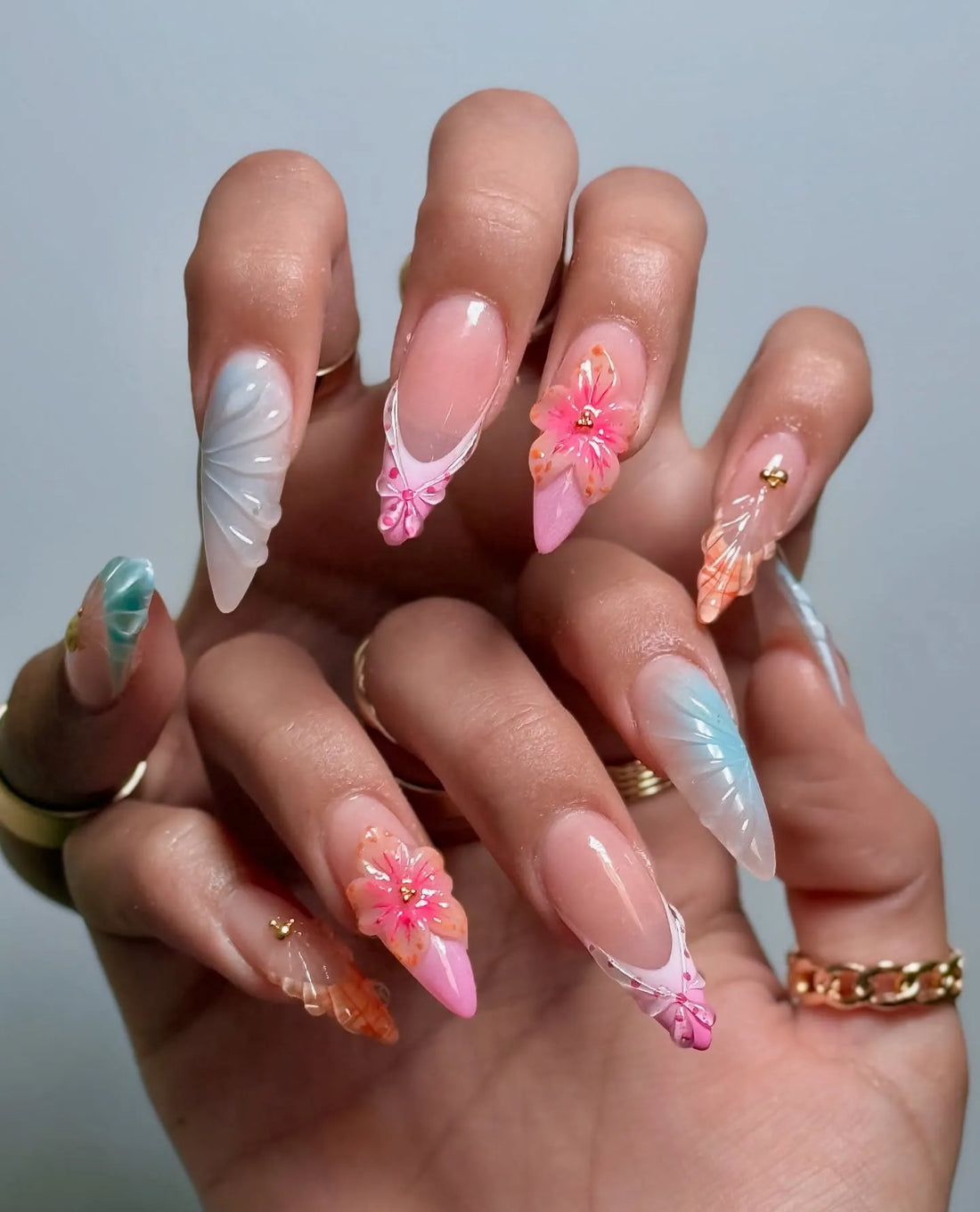 Hand wearing pastel 3D press-on nails with mermaid shell, tropical floral, and pearl accents