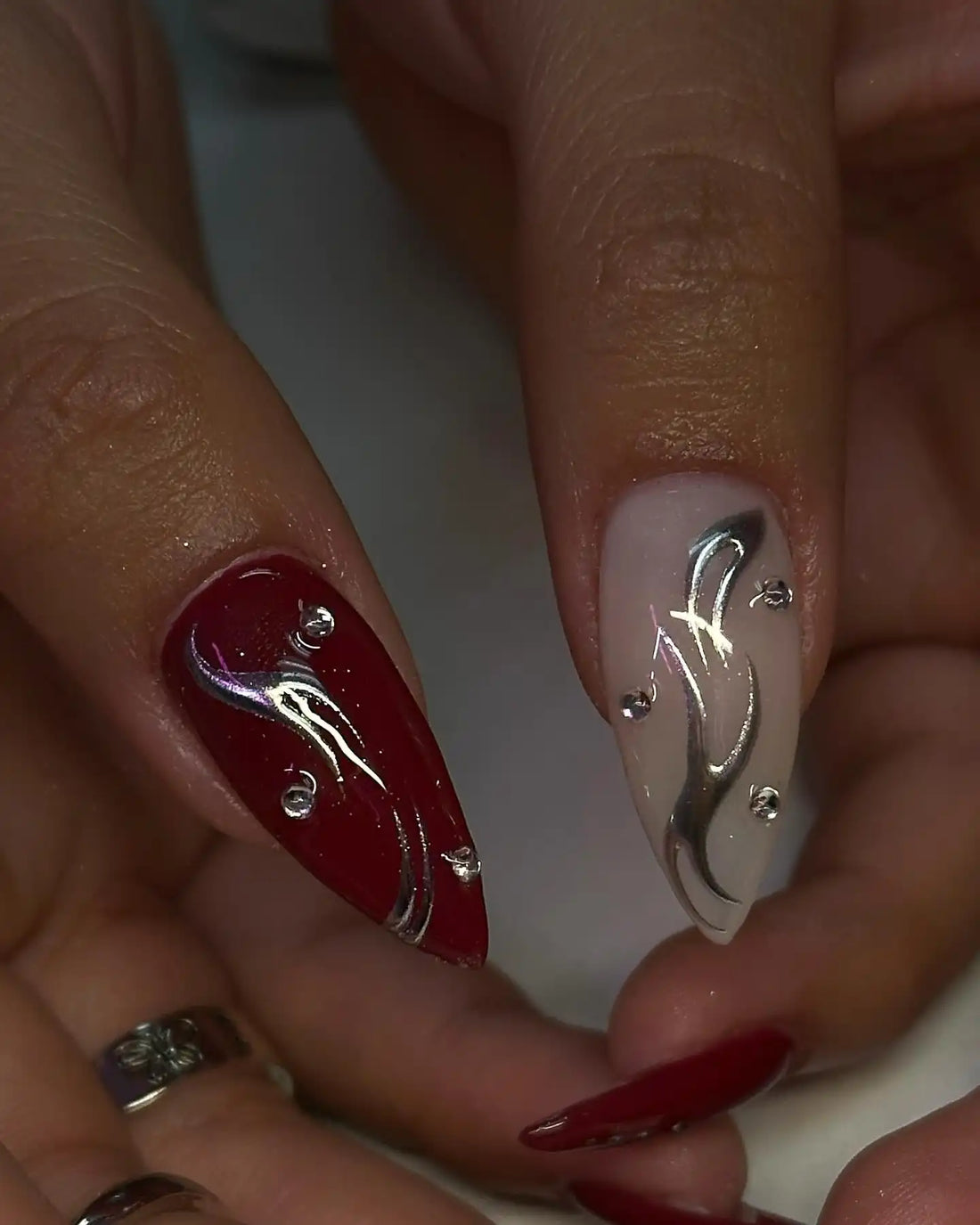 Hand with long stiletto press-on nails, red and pearl chrome with gothic heart and 3D accents.