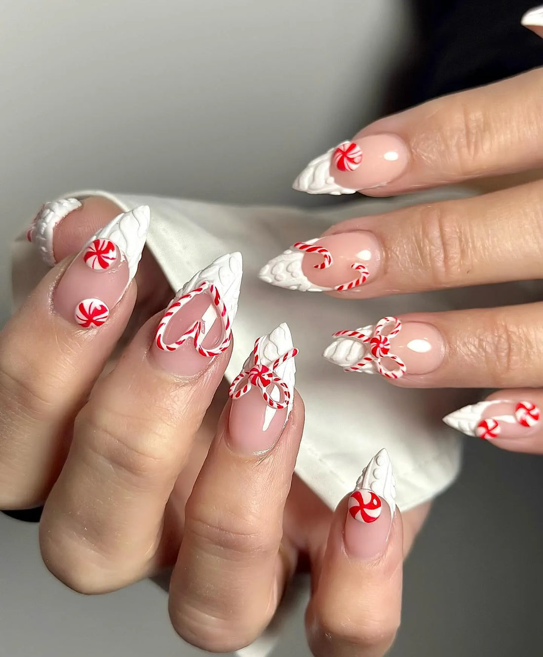 Hand with 3D holiday press-on nails featuring red and white candy cane and bow designs.