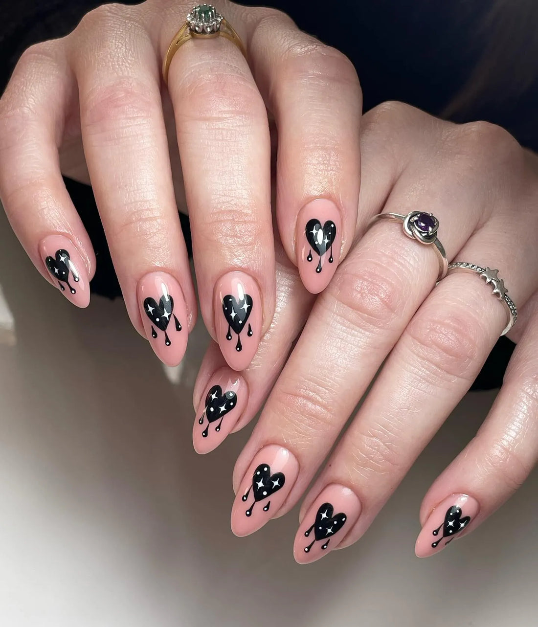 Hand wearing nude pink press-on nails with black bleeding heart and star gothic design.