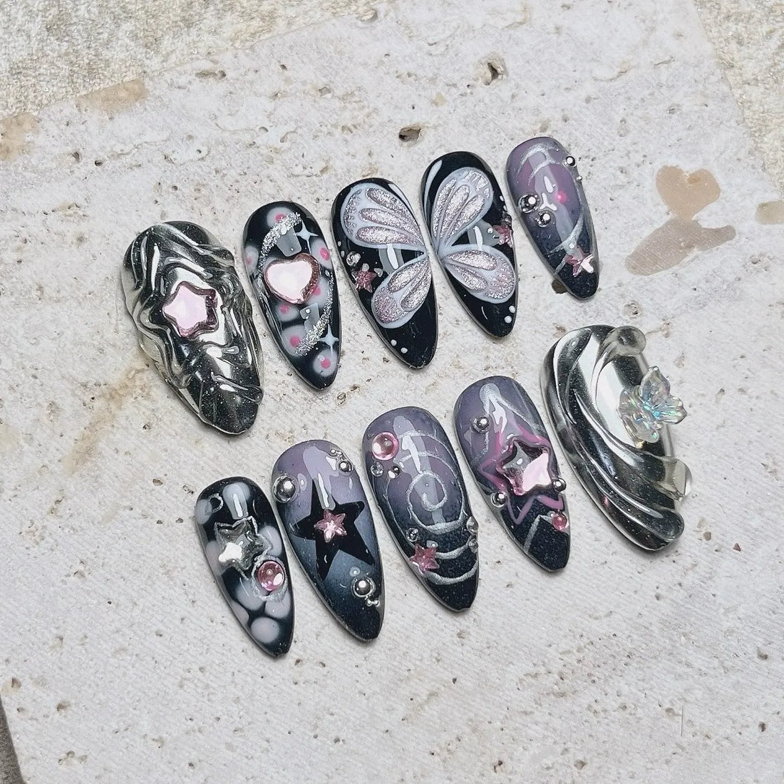 Handmade black press-on nails with silver chrome, butterfly wings, stars, and pink accents.