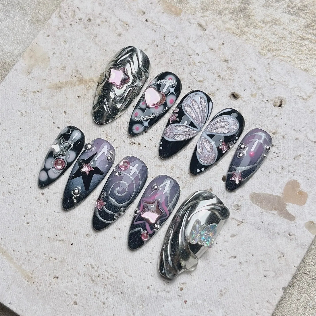 Handmade black press-on nails with silver chrome, butterfly wings, stars, and pink accents.