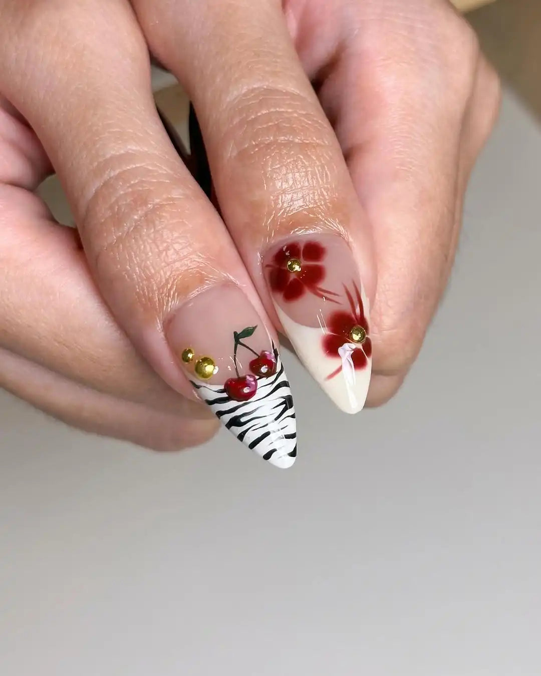 Handmade press-on nails with cherry, zebra, and red flower designs, gold studs, almond shape