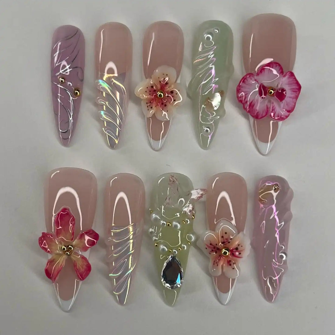 Handmade press-on nails with 3D flowers, pearls, glitter, and marble designs, arranged on a white background.