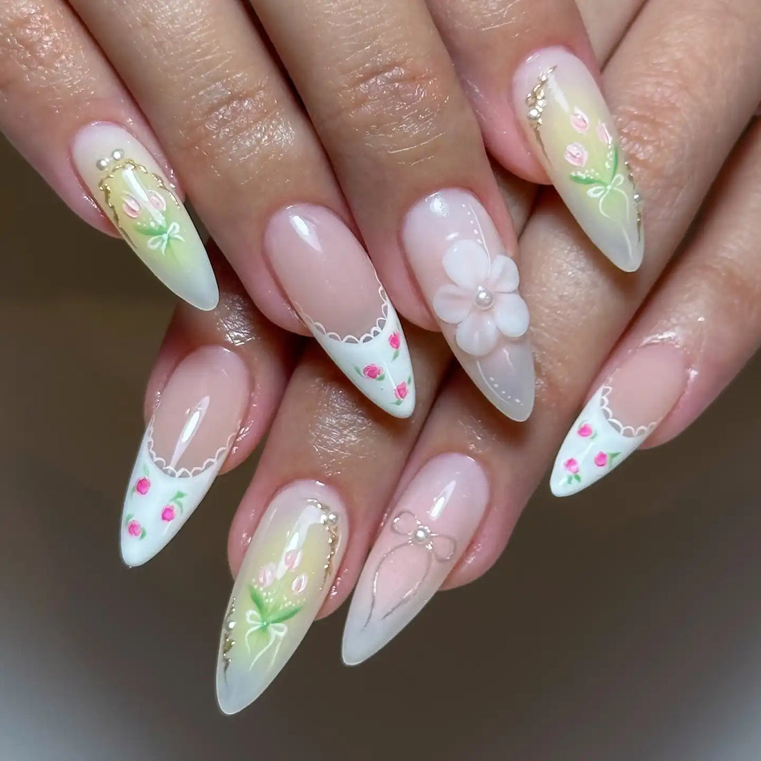 Hand with long almond-shaped press-on nails featuring pink strawberry French tips, bows, floral art, and 3D accents.
