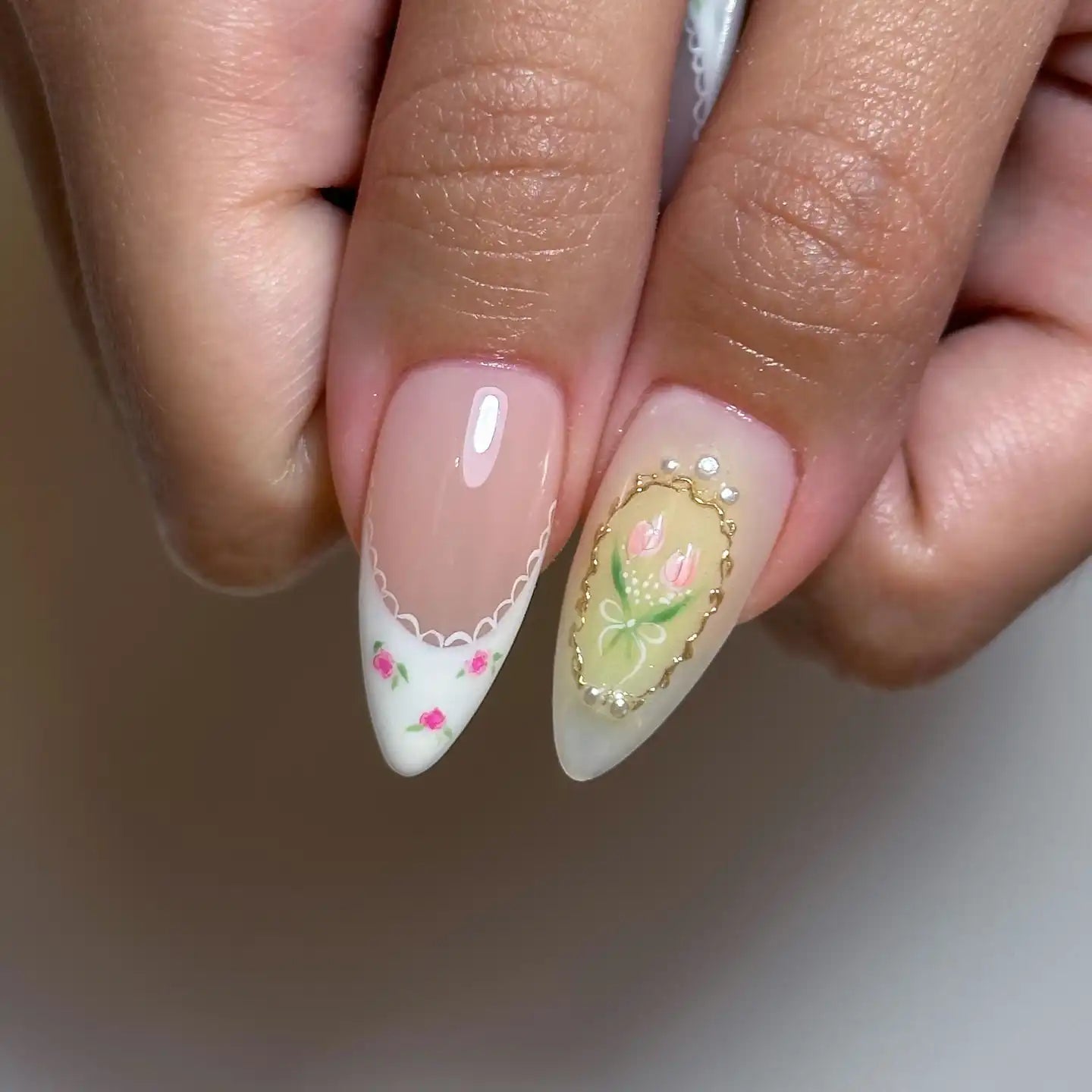 Hand holding almond-shaped fake nails with white French tips, pink floral and framed tulip art designs.