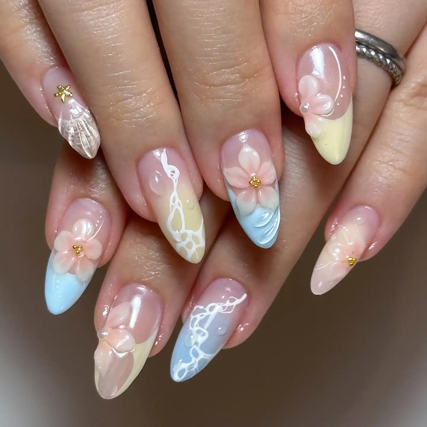 Hand with pastel blue and yellow seashell press-on nails featuring 3D floral designs