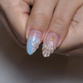 Hand holding handmade press-on nails with seashell designs, pink and blue gradient, pearl accents