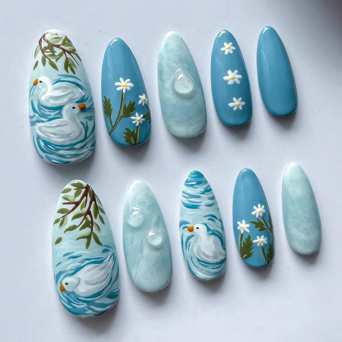 Handmade blue press-on nails with duck pond, white daisies, and spring art designs.