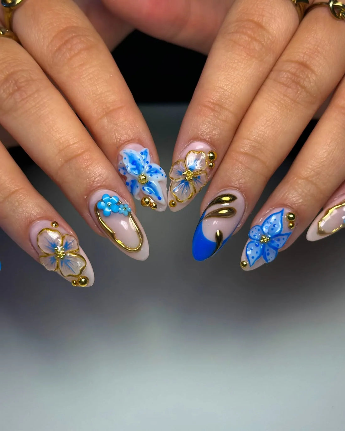 Hand with blue and gold floral 3D press-on nails, featuring bohemian luxe design.