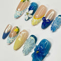 Handmade blue and yellow press-on nails with 3D floral and lemon designs on white background