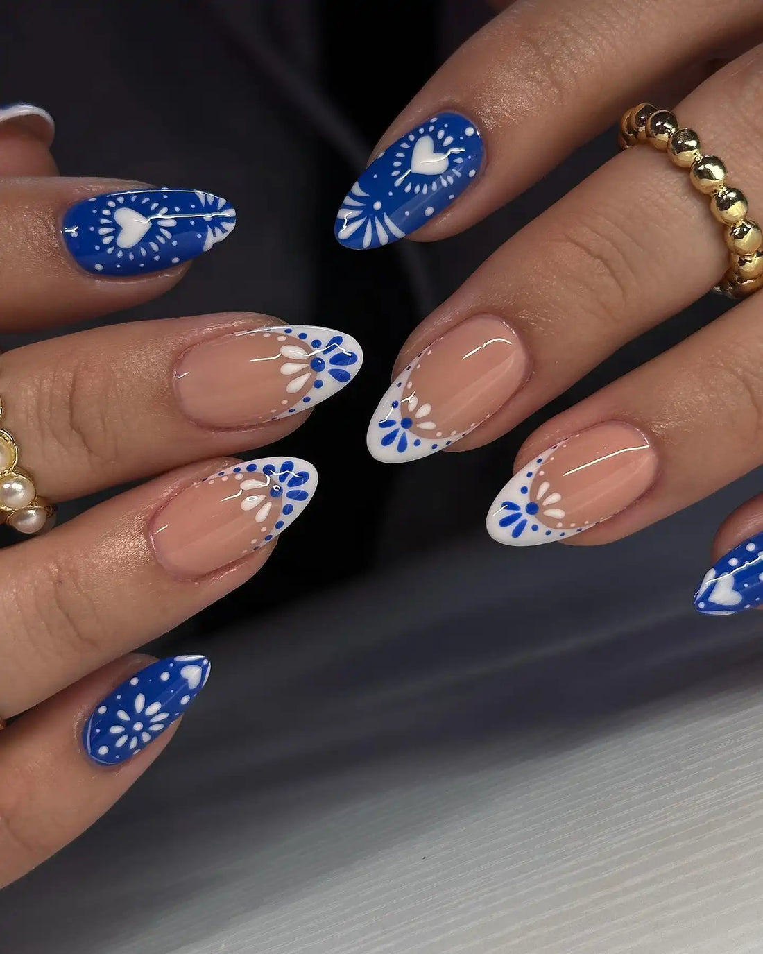 Handmade blue and white press-on nails with heart and floral designs, almond shape