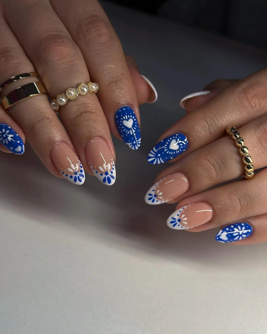 Handmade blue and white press-on nails with heart and floral designs, almond shape