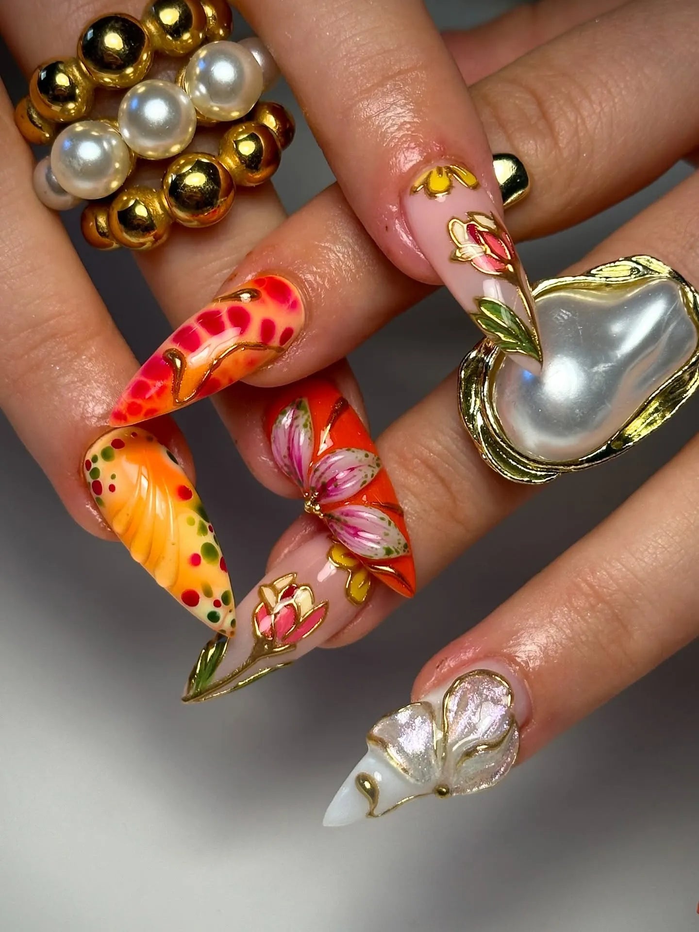 Hand with bold red, orange, and gold 3D floral butterfly press-on nails, luxury design.