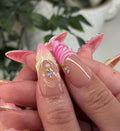 Handmade pink press-on nails with floral seashell designs and sparkling gems.