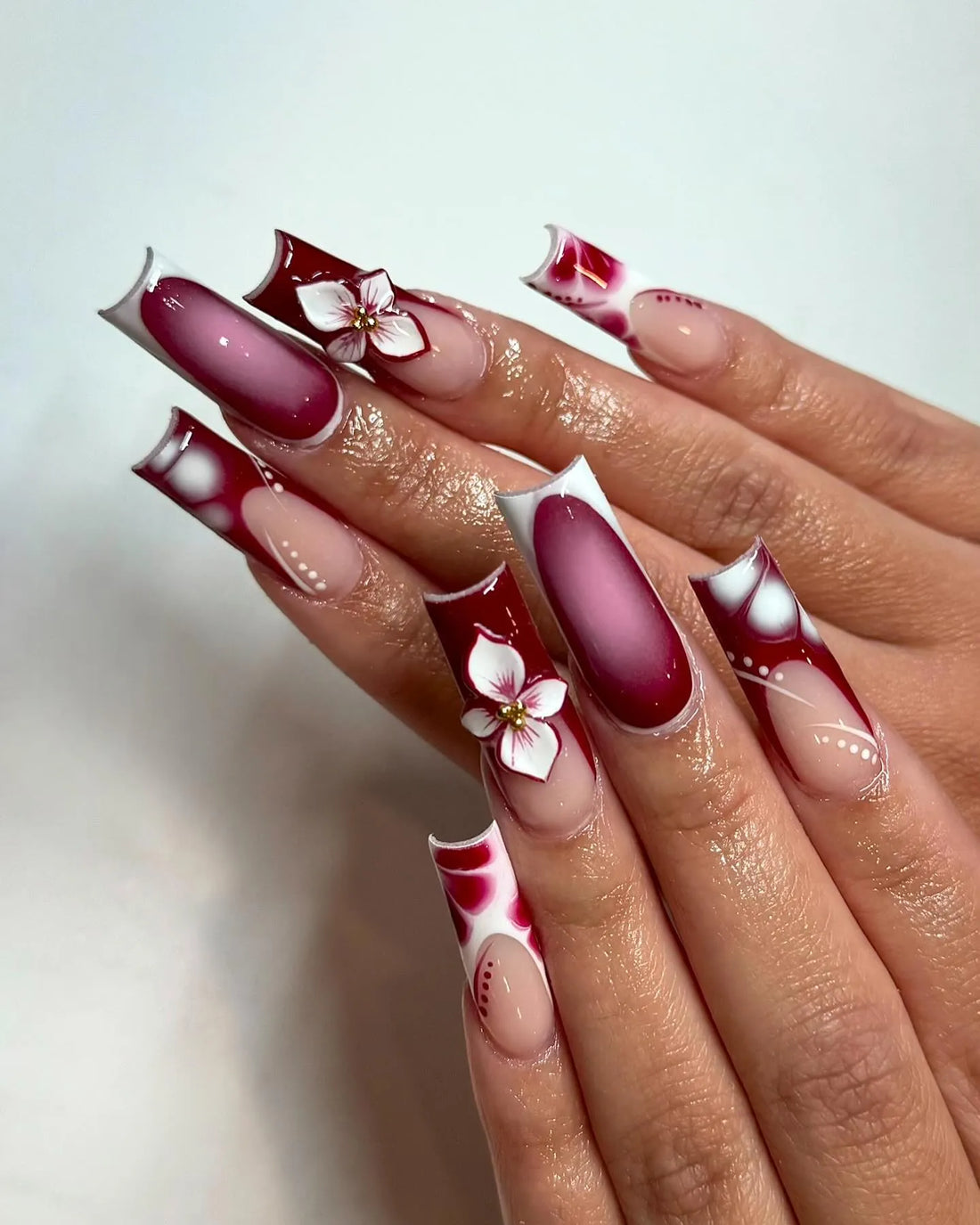 Hand with long burgundy ombre abstract French tip press-on nails and 3D floral accents