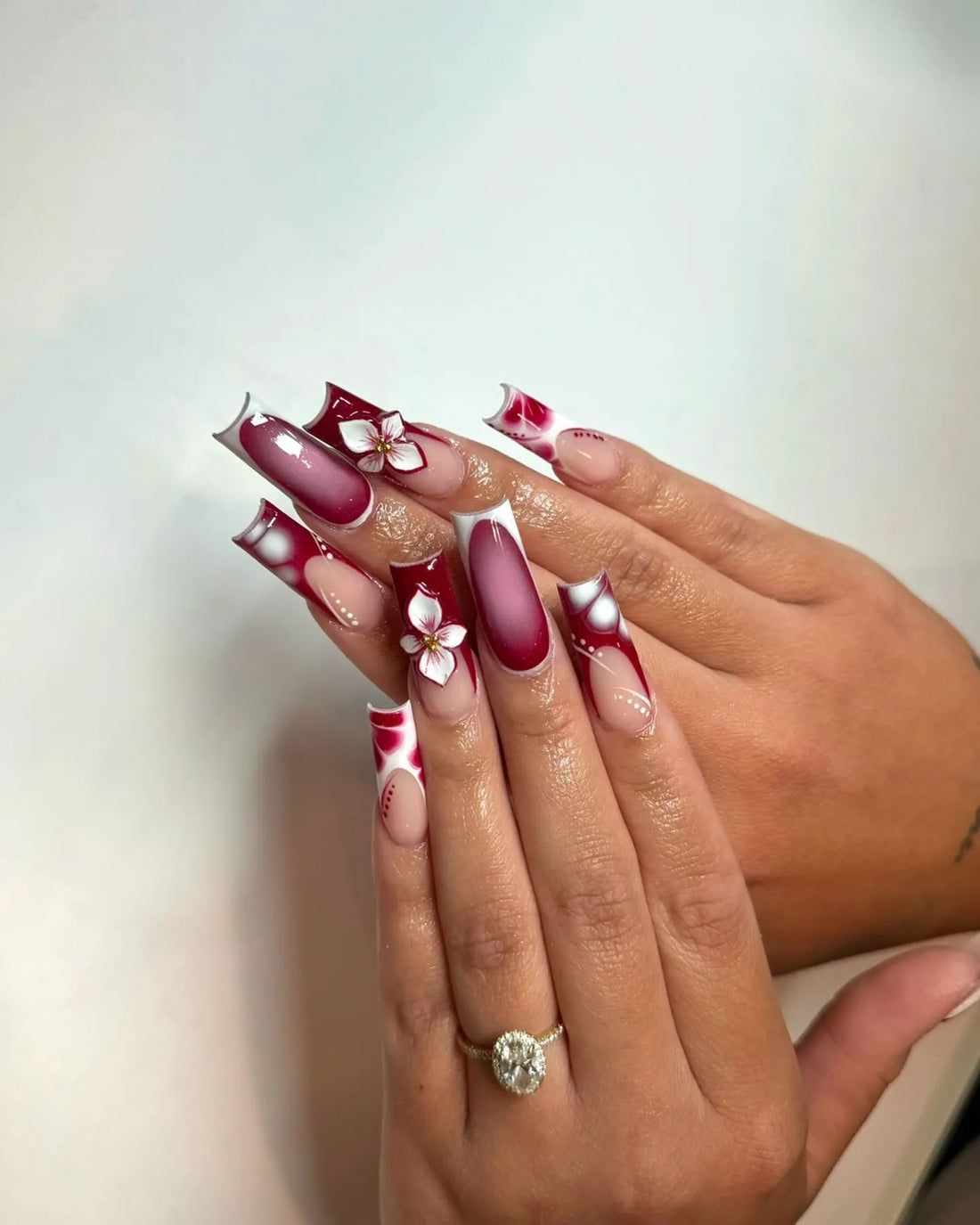 Hand with long burgundy ombre abstract French tip press-on nails and 3D floral accents