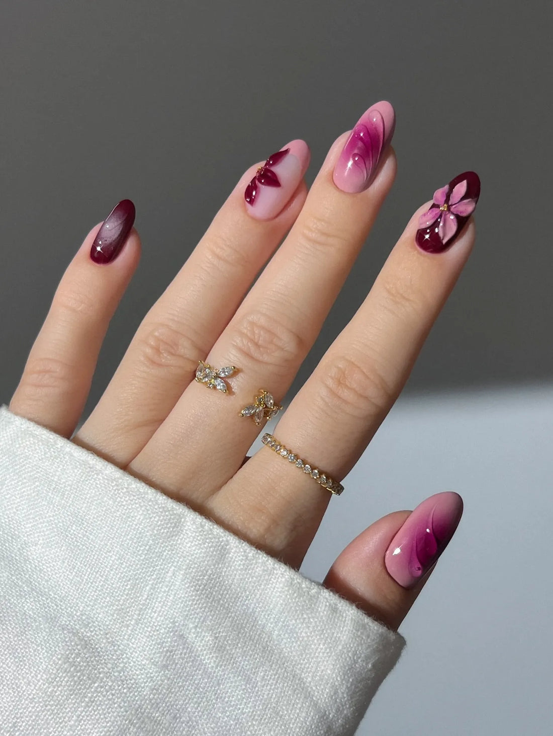 Hand with handmade burgundy and pink ombre press-on nails featuring 3D floral designs.