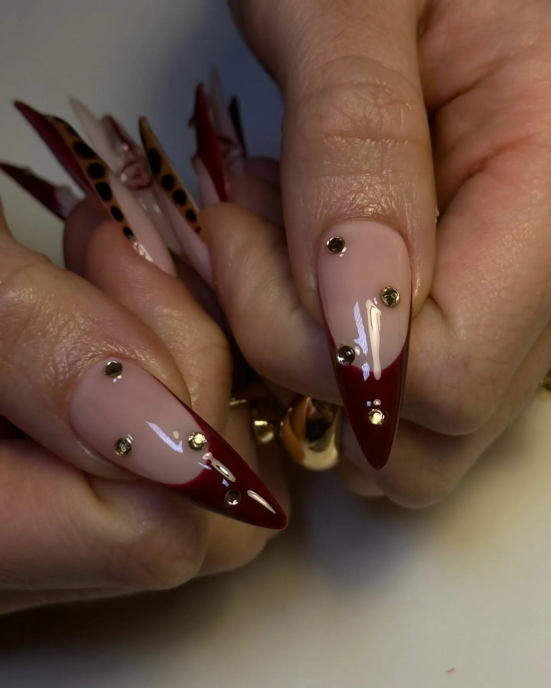 Hand with long stiletto press-on nails in burgundy red, leopard print, and 3D floral designs.