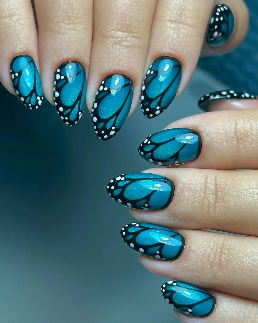 Handmade press-on nails with teal butterfly wing design and white dot accents