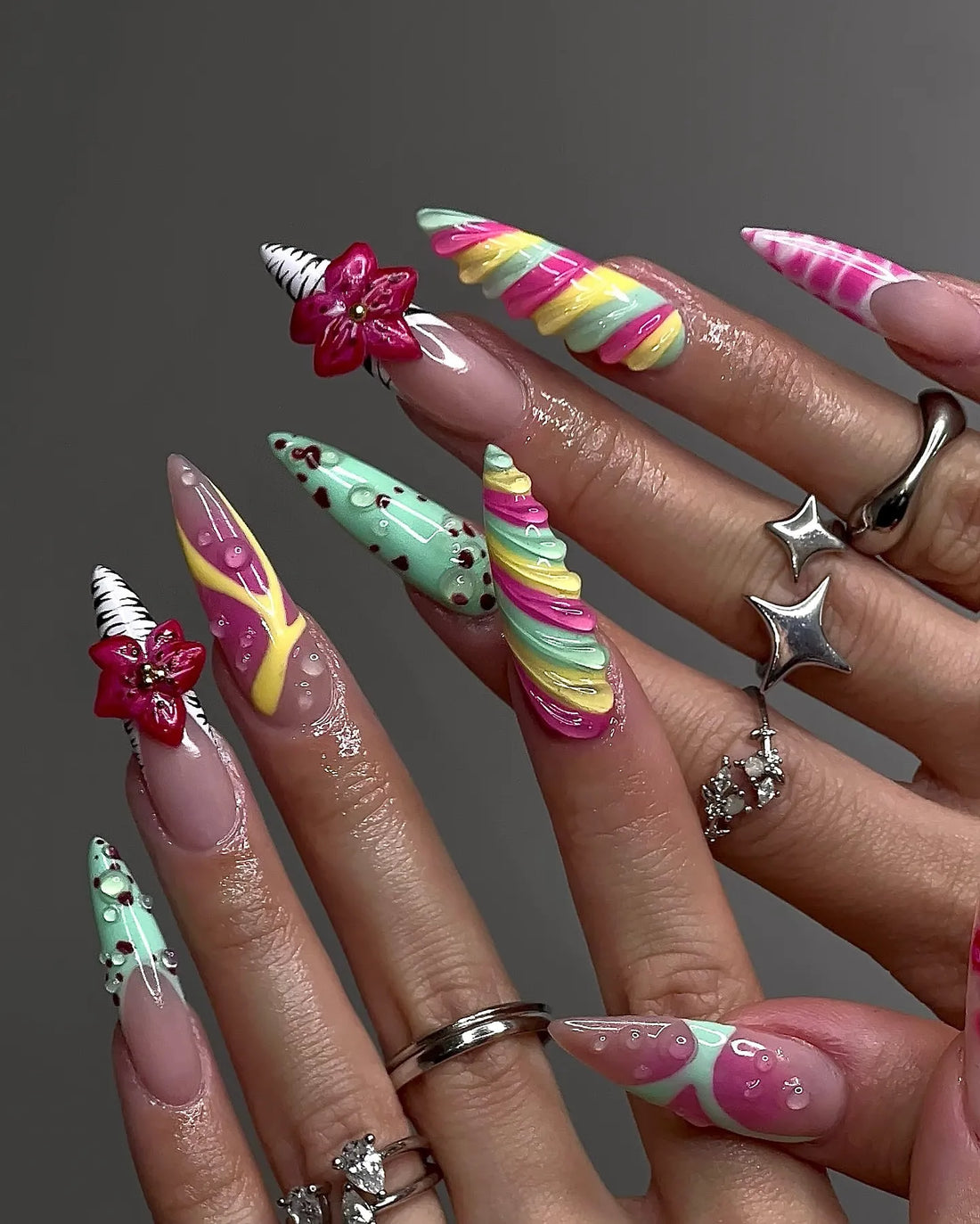 Hand with long handmade press-on nails featuring colorful candy swirl, 3D flowers, and quirky designs.