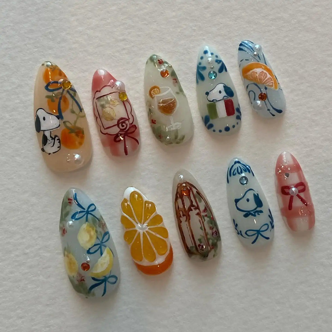Handmade press-on nails with cartoon dog, citrus fruit, wine glass, and ribbon designs.