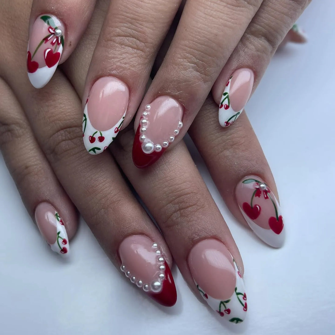 Handmade press-on nails with cherry French tips, red accents, and pearl embellishments.