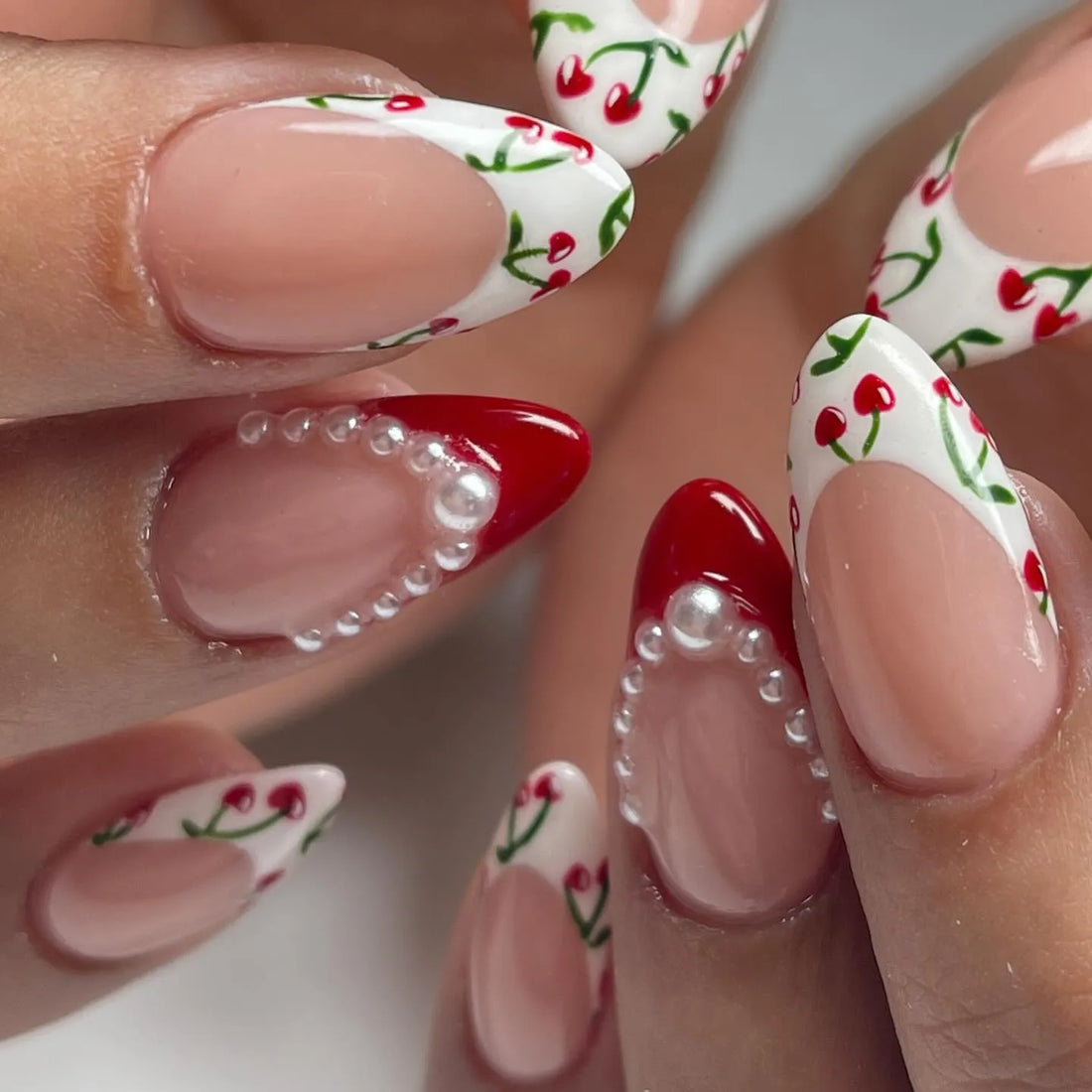 Handmade press-on nails with cherry French tips, red accents, and pearl embellishments.
