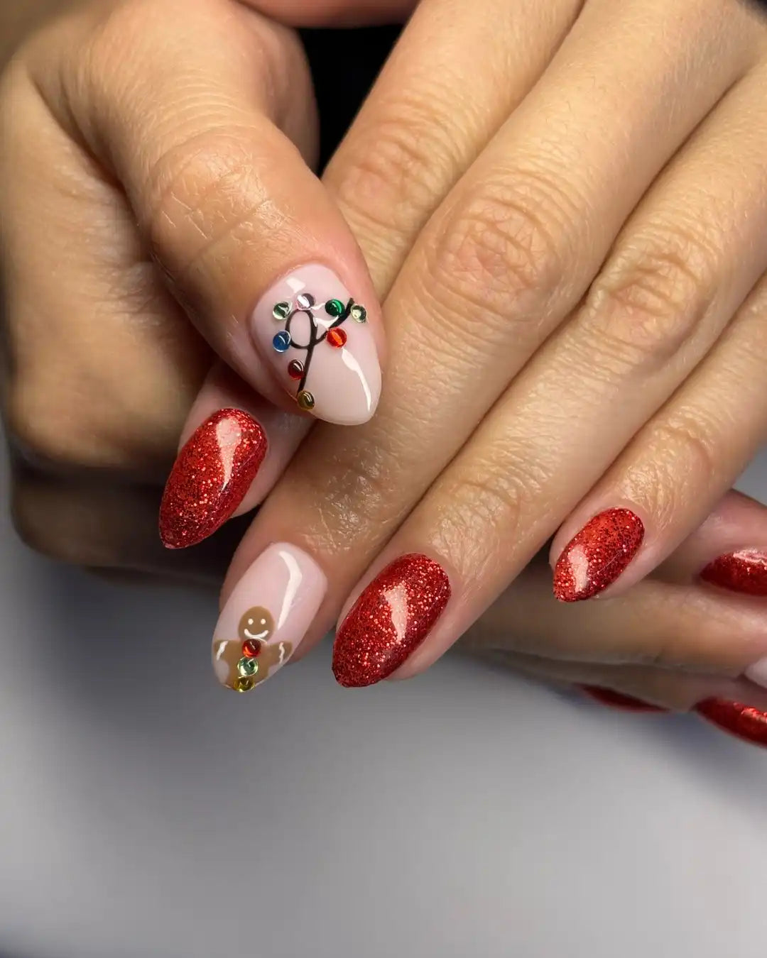 Hand with red glitter Christmas press-on nails, gingerbread and festive light designs.