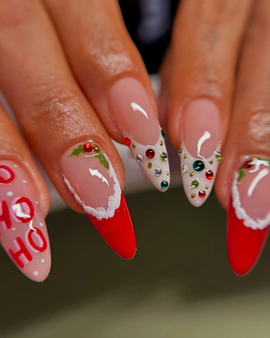 Hand with Christmas press-on nails featuring red tips, holly, and HO HO HO festive designs.