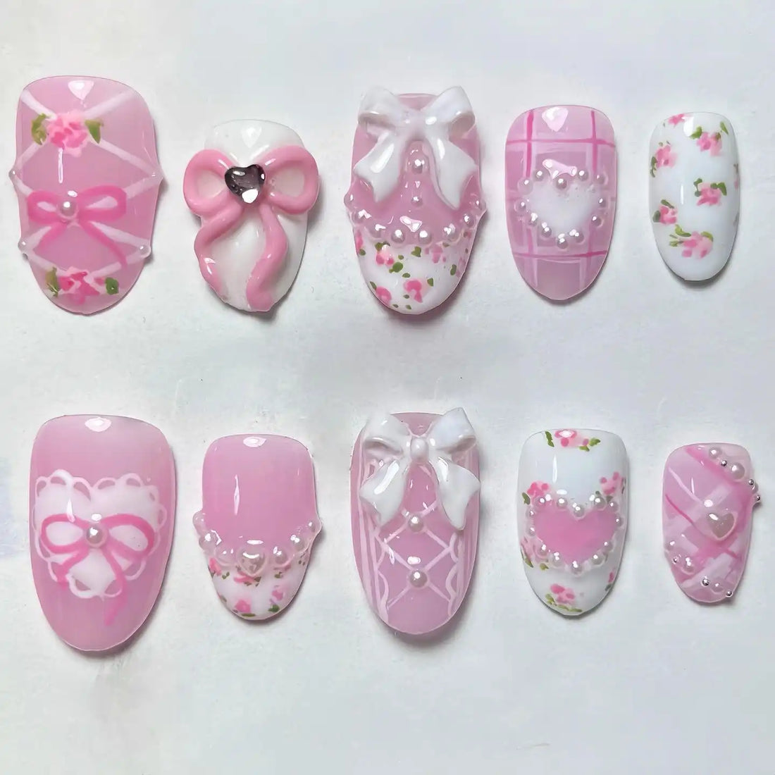 Handmade pink press-on nails with floral designs, bows, pearls, lace, and heart accents.