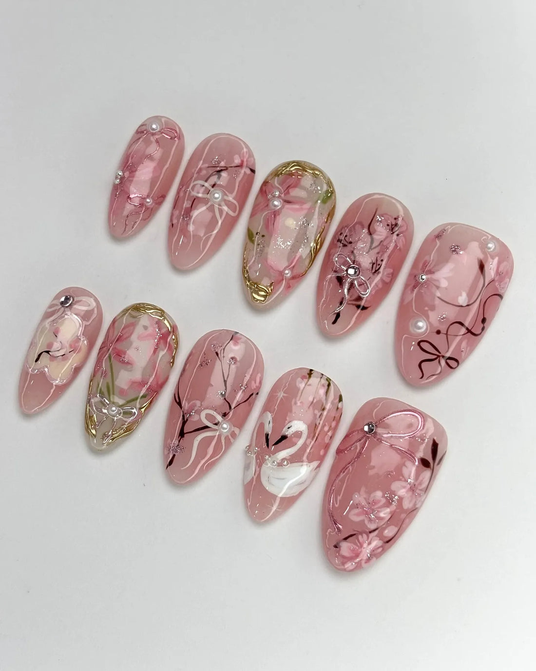 Handmade pink press-on nails with cherry blossom, ribbon, swan, and pearl accents.