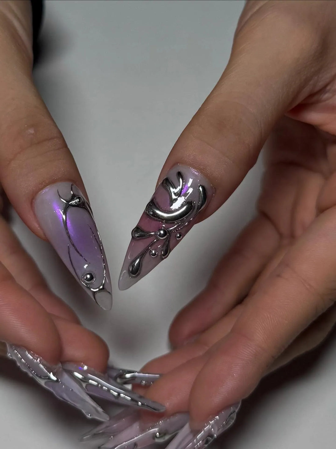 Hand with long coffin-shaped press-on nails in metallic lavender ombre, silver chrome cyberpunk design