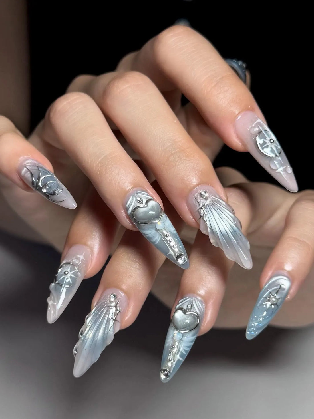 Hand with long stiletto silver press-on nails featuring heart and celestial 3D designs
