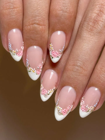 Handmade pink floral French tip press-on nails with pearl accents on natural hands
