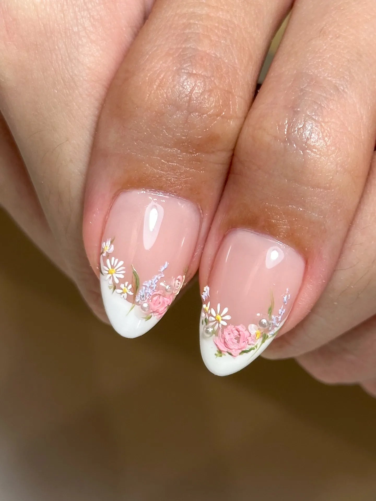 Hand with pink floral French tip press-on nails, featuring pearl and garden flower accents.
