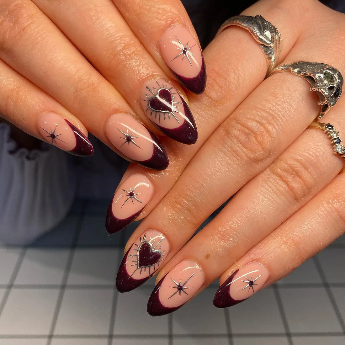 Handmade almond press-on nails with dark burgundy French tips, silver hearts, and star accents