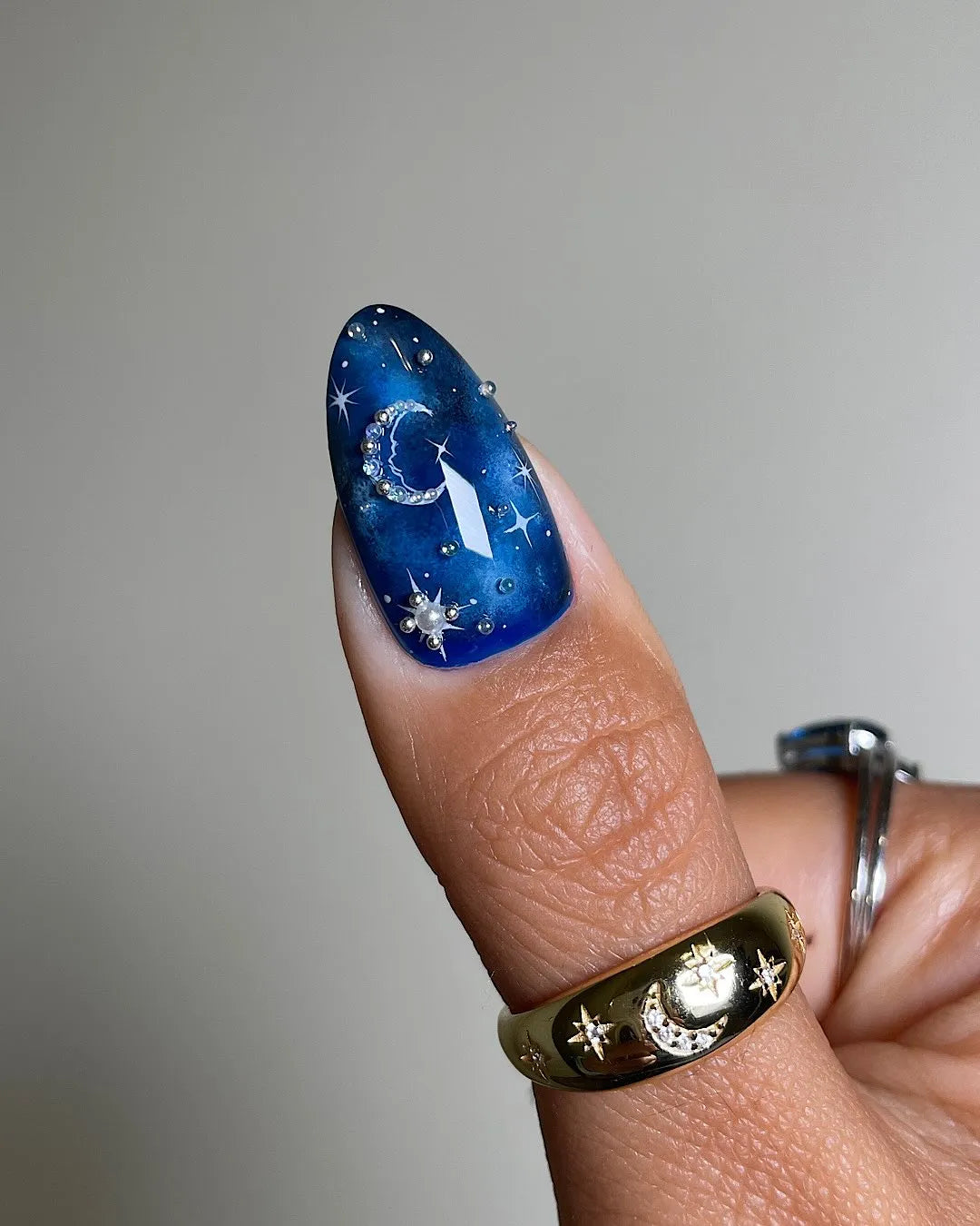 Hand with deep blue galaxy press-on nails featuring sparkling stars and moon designs.