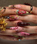 Hand with handmade deep red press-on nails featuring 3D floral designs and gemstone accents.