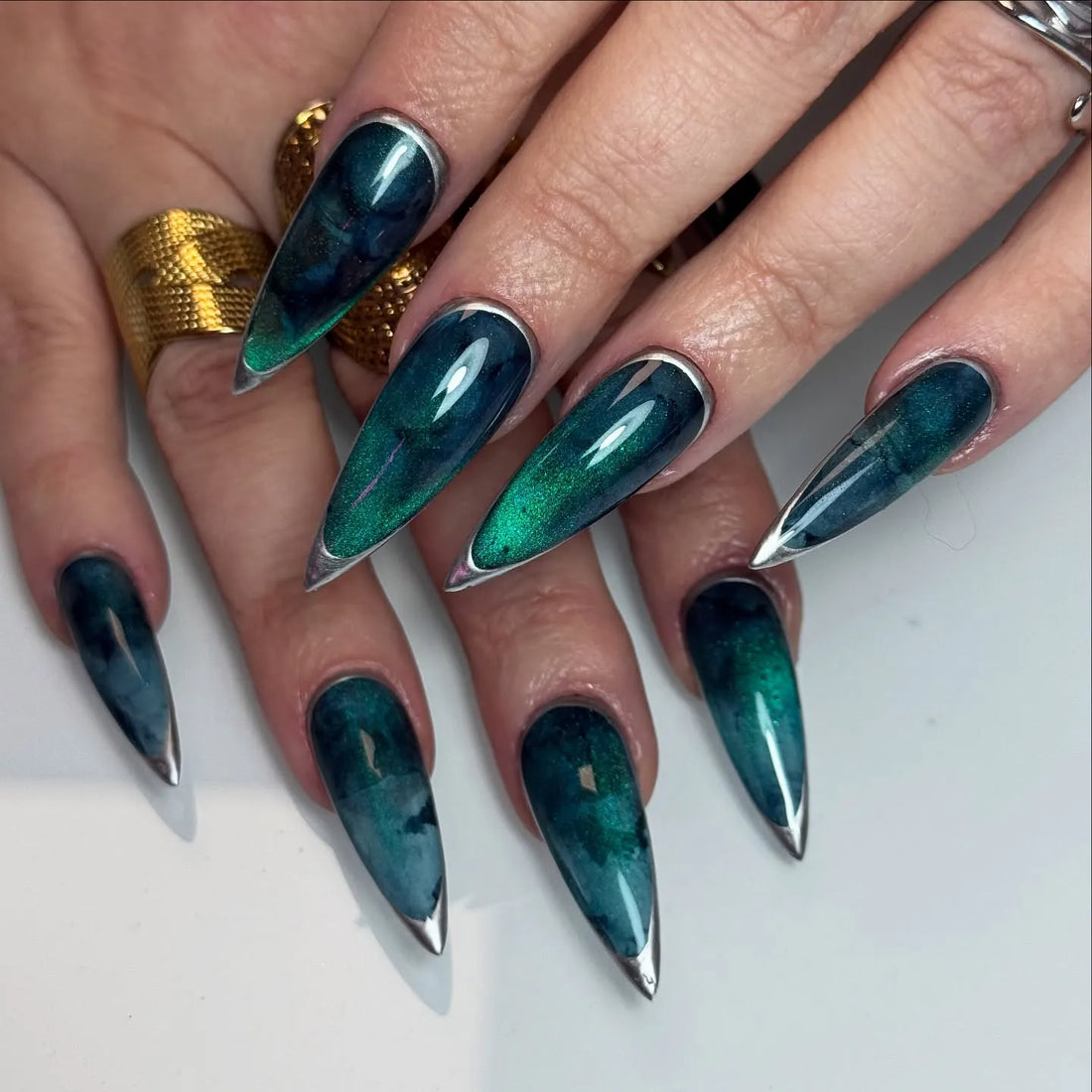 Handmade deep teal nebula press-on nails with silver metallic pointed tips, stiletto shape