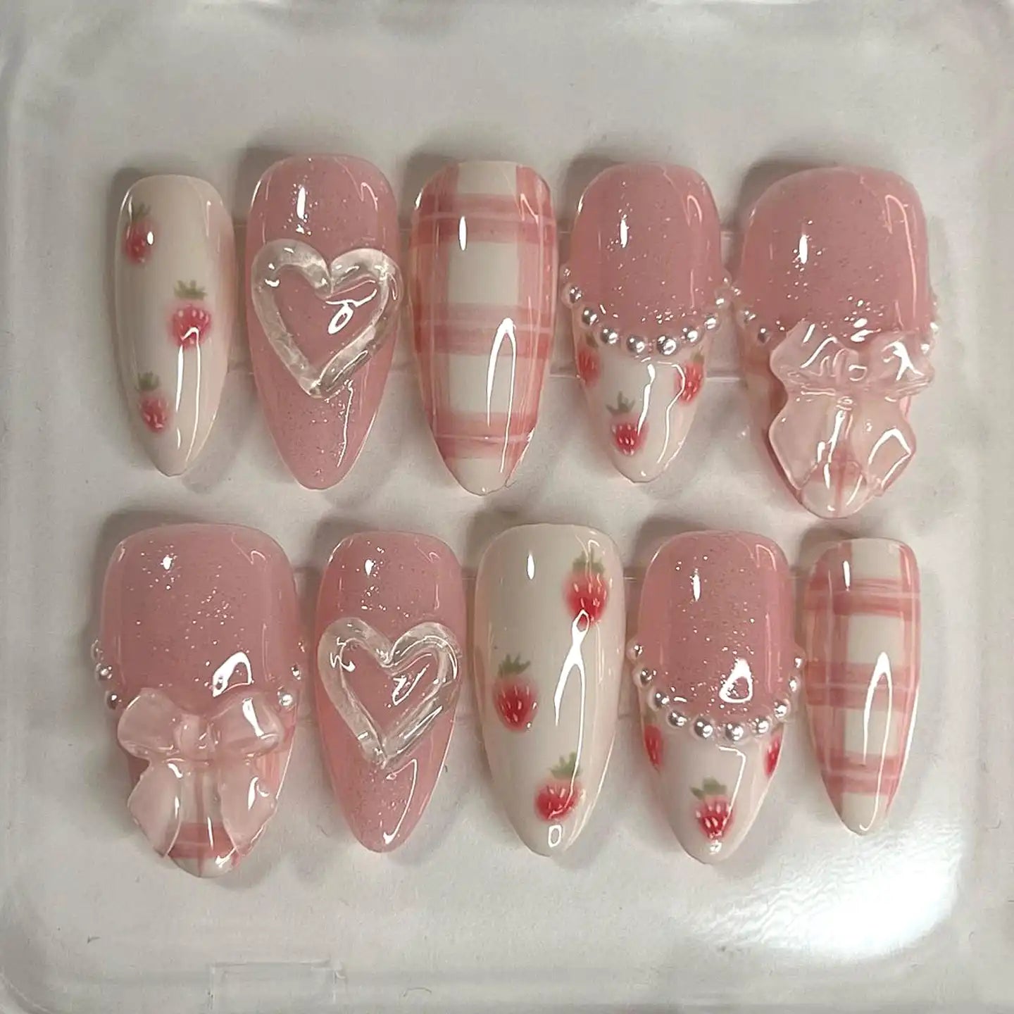 Handmade pink press-on nails with bows, hearts, pearls, plaid, and strawberry designs