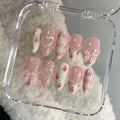 Handmade pink press-on nails with bows, hearts, strawberries, plaid and pearl accents in a case.