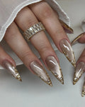 Hand modeling metallic taupe stiletto press-on nails with gold chrome edges and rhinestones.