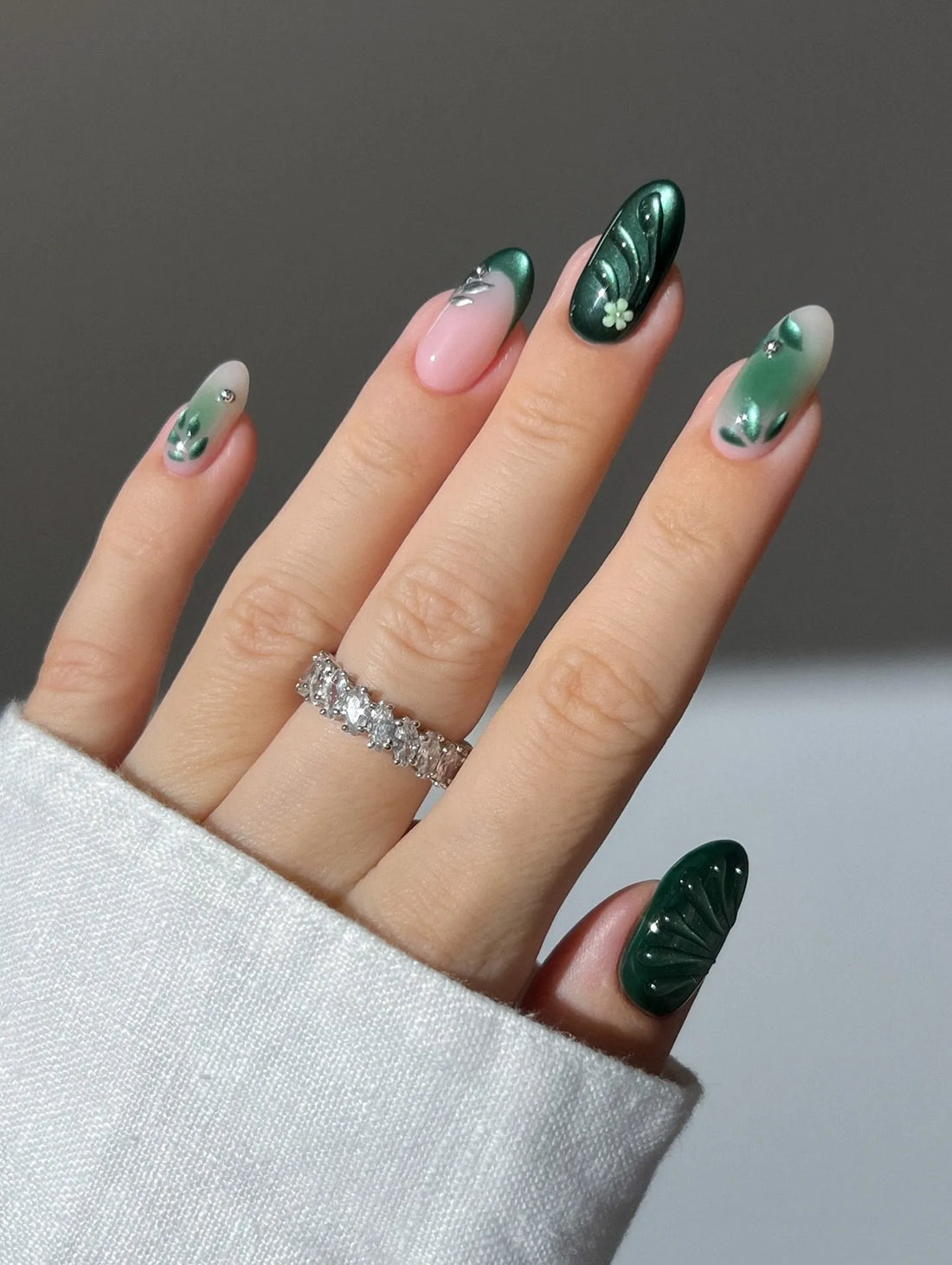 Hand with emerald green botanical leaf swirl press-on nails and floral accents