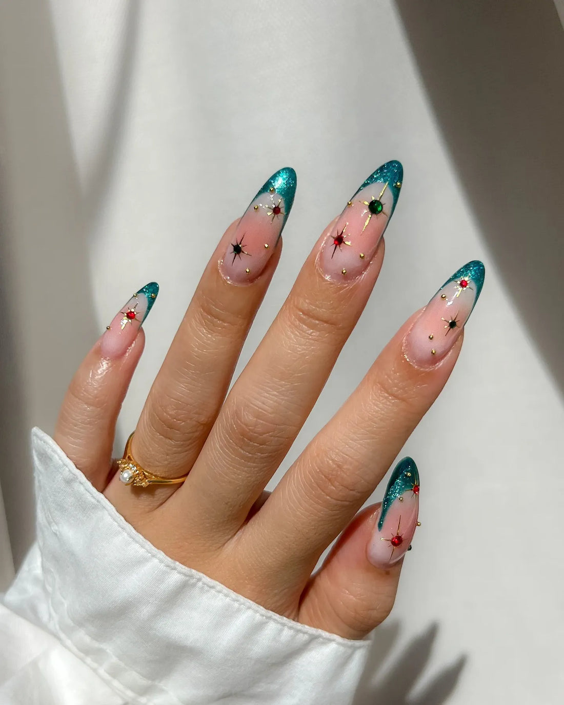 Hand with emerald green French tip press-on nails featuring gold studs and star jewel accents.